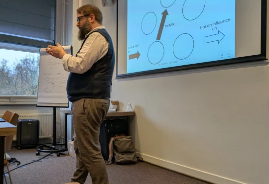 Jonathan Shubs explaining at the flip chart, beside a slide on tonifying and how the elements influence each other