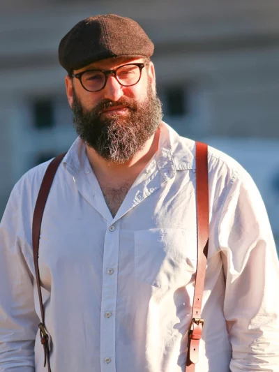 Jonathan Shubs, standing outdoors in warm light, wearing a cap and a white shirt